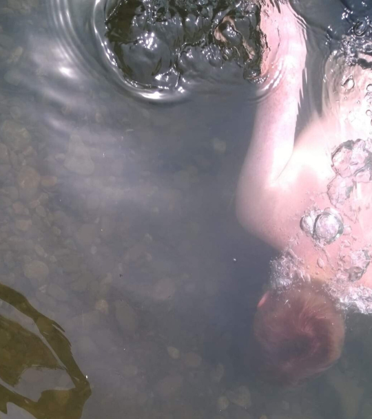 Aerial view of a boy swimming under water with bubbles flowing out behind him