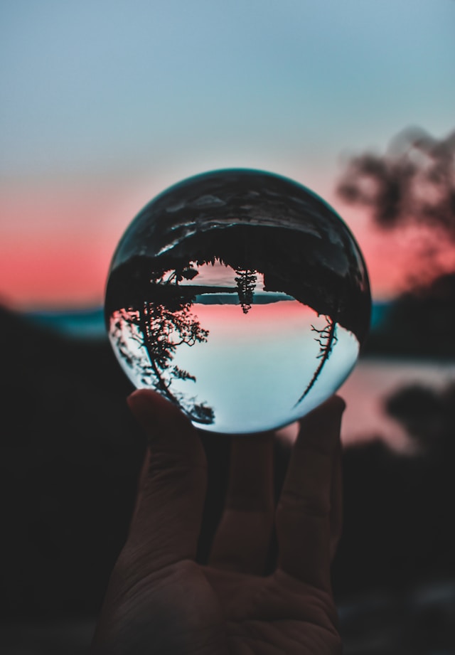 a hand holds a crystal ball reflecting an upside lake and trees